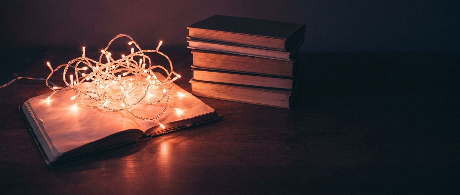 Warm string lights spilling from an open notebook beside a stack of books